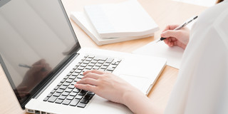 Young woman in profile sitting at open laptop at table, books next to it