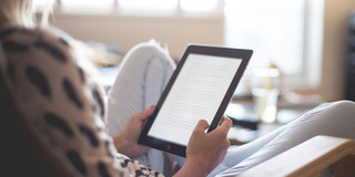 Woman reading e-book A Woman is sitting in an armchair and reading an e-book